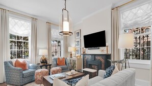 A well-lit living room with a fireplace, comfortable seating, and large windows.