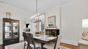 A dining room with a dark wooden table, six chairs, a chandelier, a glass cabinet, and a fireplace.