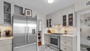 A modern kitchen with white cabinetry, a stainless steel refrigerator, an oven, and a countertop with a coffee maker.