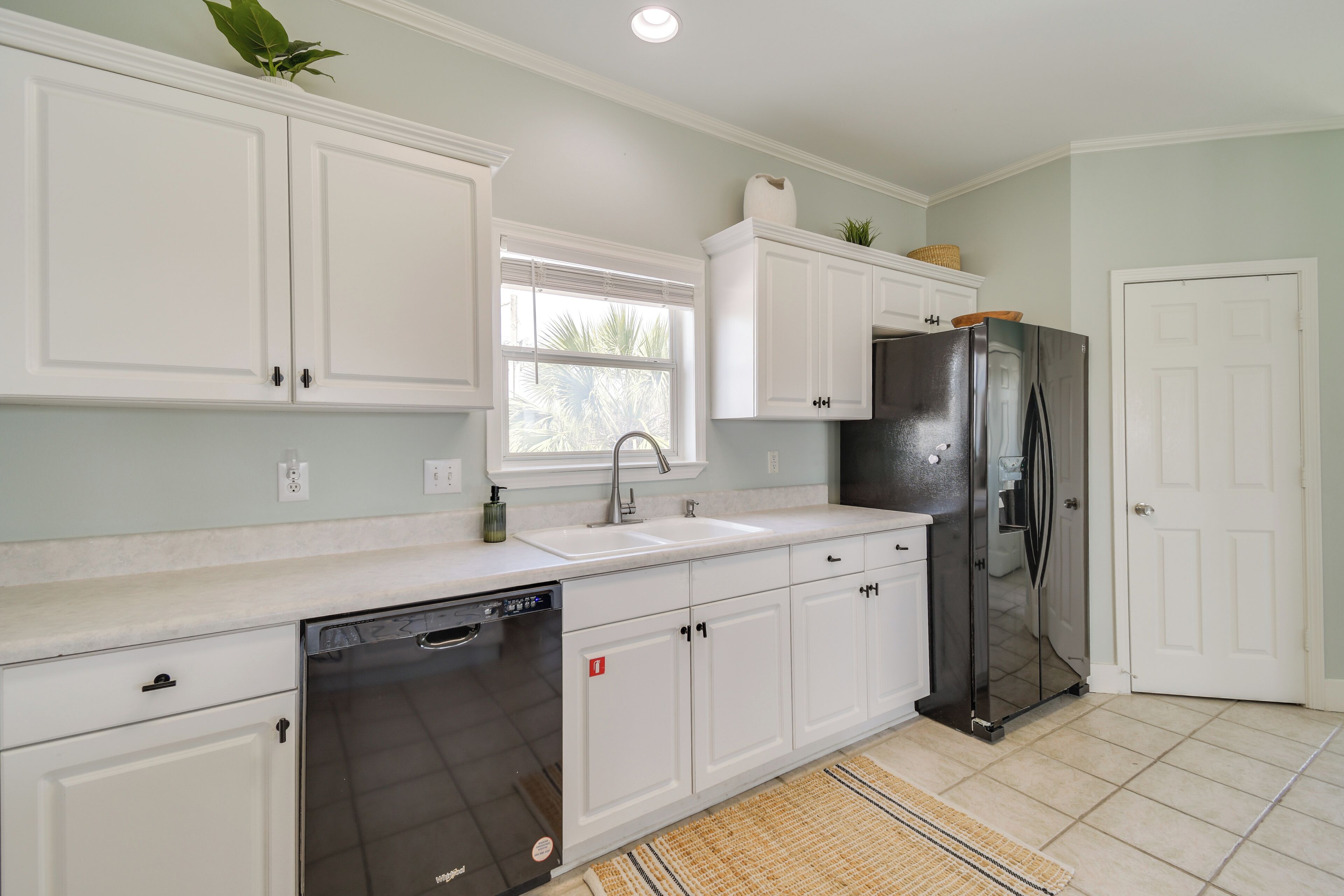 A kitchen with white cabinets, a dishwasher, a refrigerator, and a window with blinds.