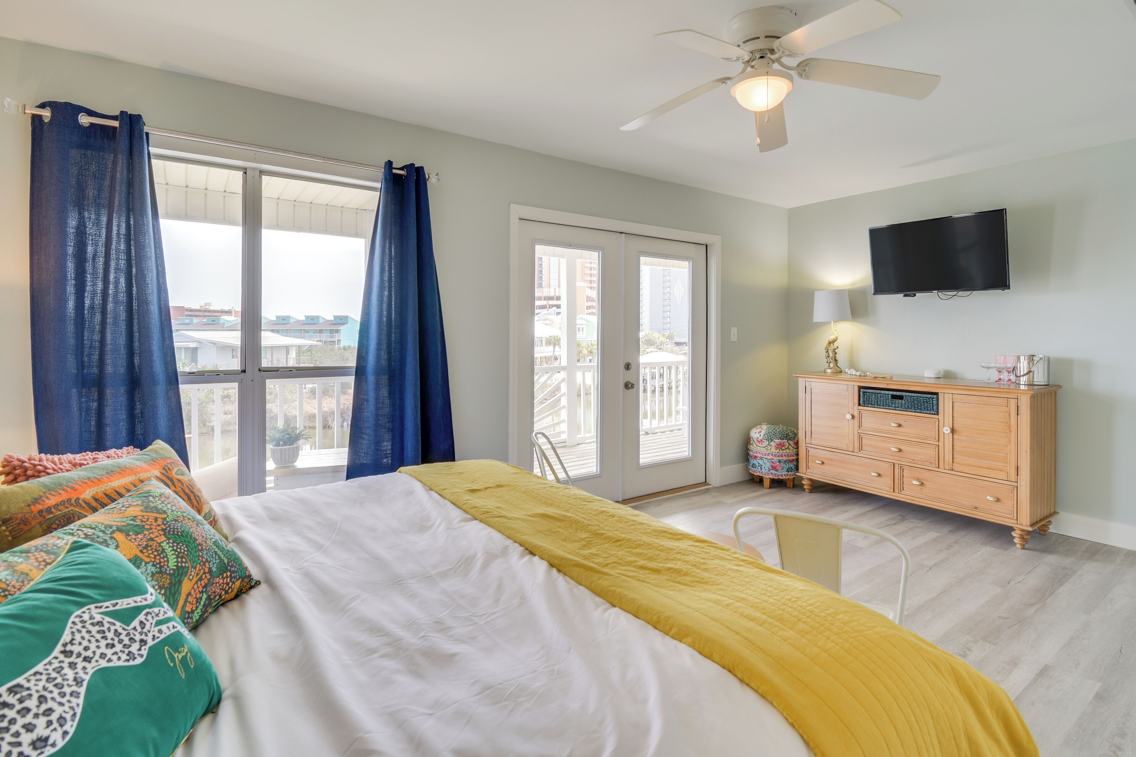 A bedroom with a bed, a dresser, a television, and a balcony with curtains.