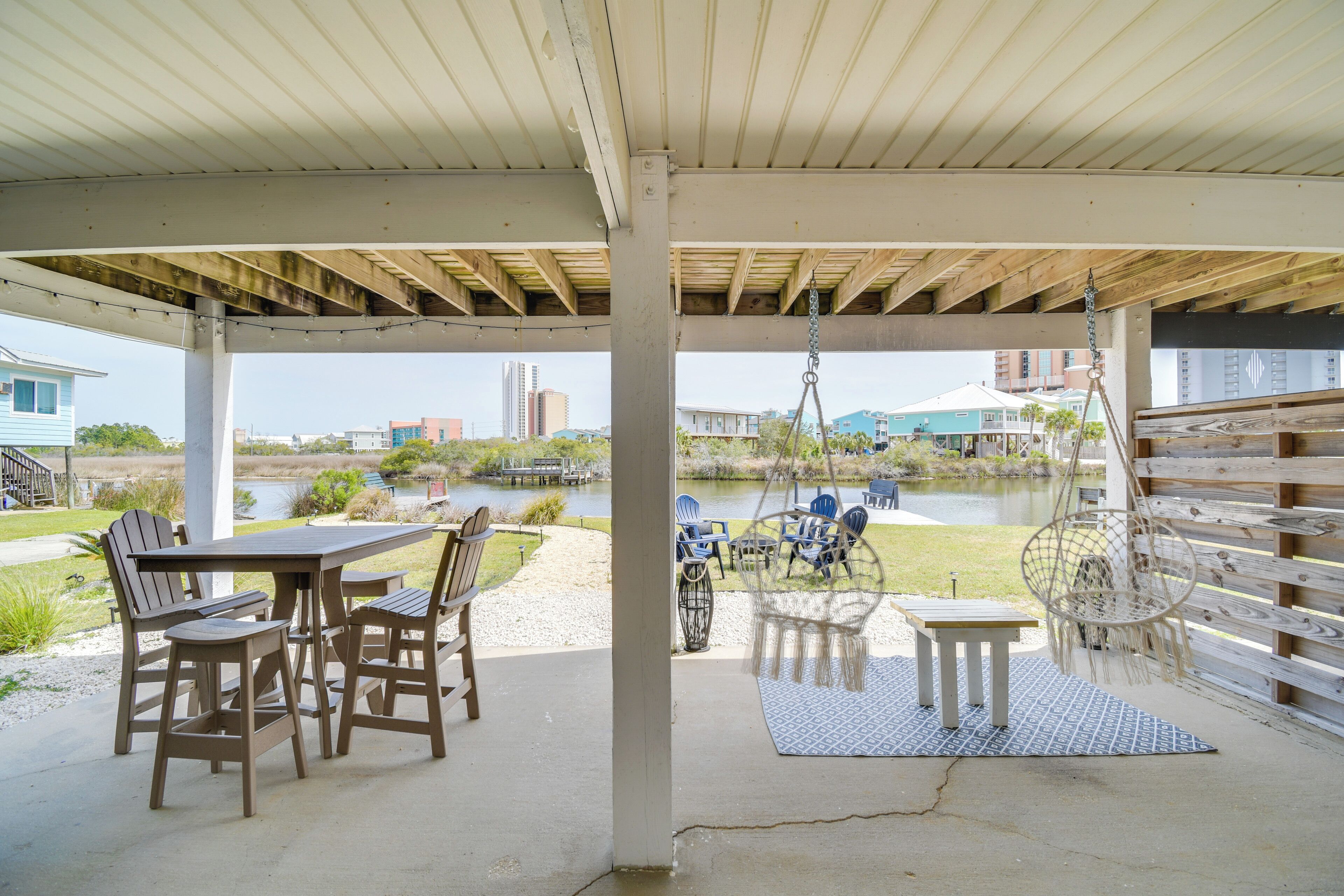 An outdoor patio with a table and chairs, a hanging chair, and a view of a body of water and buildings in the distance.