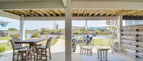An outdoor patio with a table and chairs, a hanging chair, and a view of a body of water and buildings in the distance.