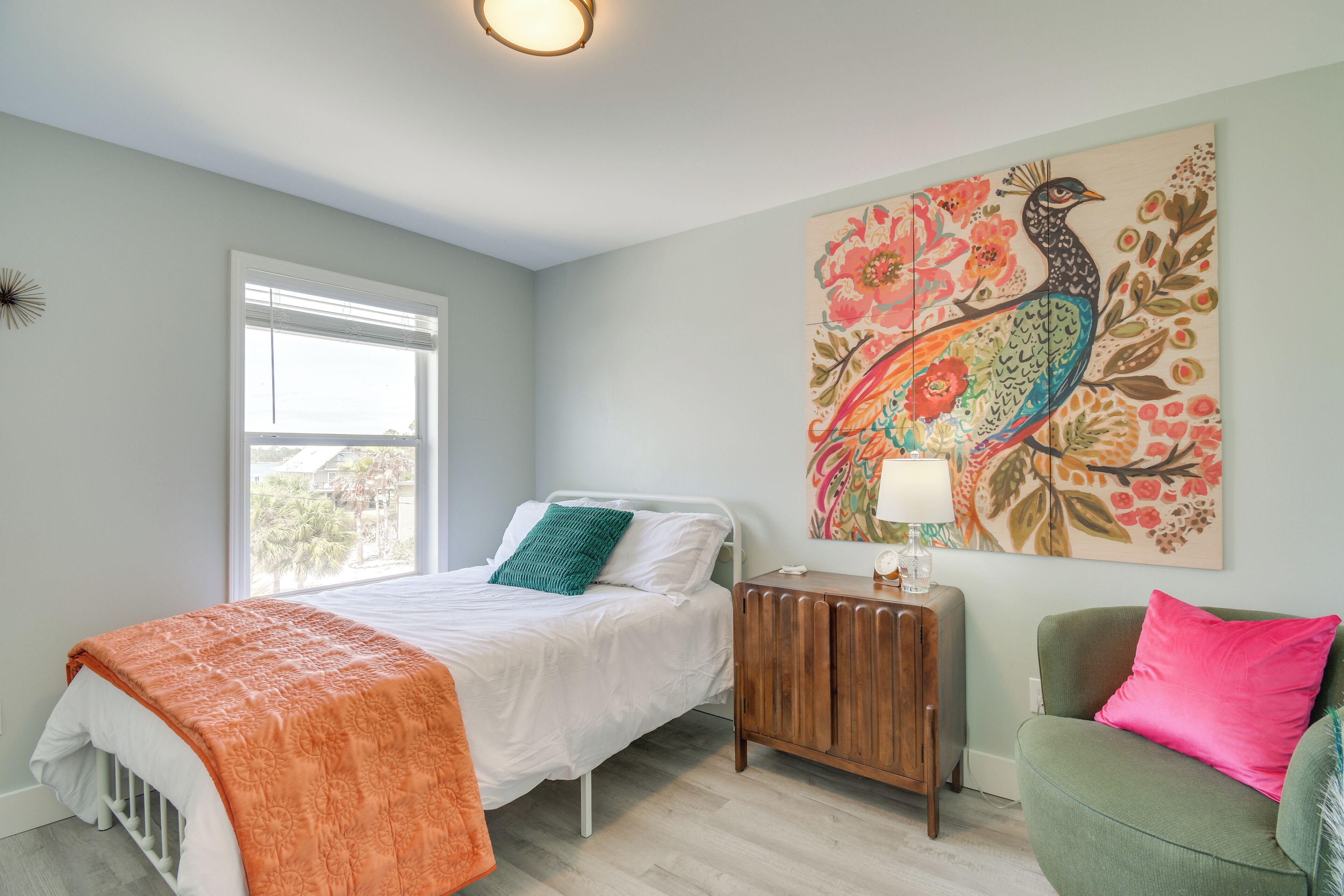 A bedroom with a bed, bedside table, lamp, and a colorful wall painting.