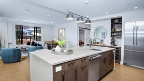 A modern kitchen with a central island, stainless steel appliances, and a dining area with blue chairs. - New Mtn Modern with Luxurious Amenities | F213 (Avon)