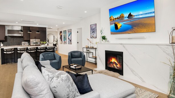 A modern living room with a fireplace, a large flat-screen TV, and a kitchen in the background. - New Mtn Modern with Luxurious Amenities | F213 (Avon)