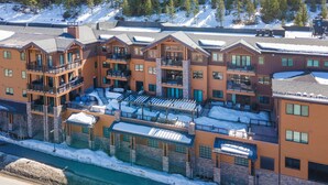 A multi-story hotel with balconies, a ski slope in the background, and a snow-covered ground. - New Mtn Modern with Luxurious Amenities | F213 (Avon)
