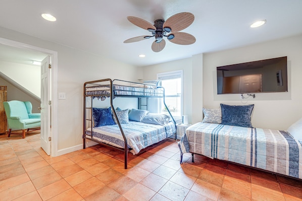 Un dormitorio con una cama litera, una cama individual, un ventilador de techo y un ventanal grande.