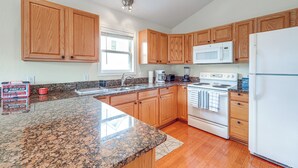 Una cocina con armarios de madera, encimeras de granito, microondas, estufa y refrigerador.
