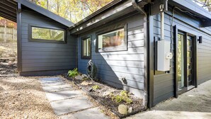 Uma casa moderna com fachada cinzenta, um caminho de pedra que leva à entrada e um pequeno jardim com plantas e uma mangueira.