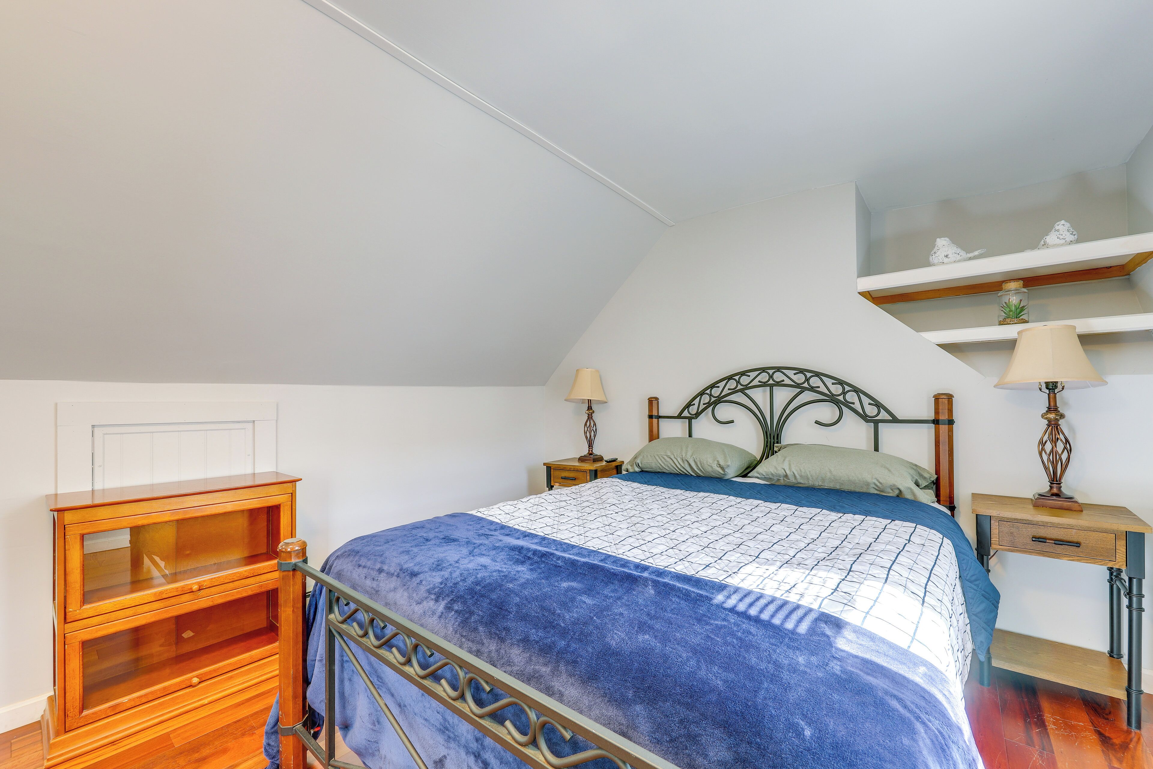 A bedroom with a bed, wooden nightstands, a dresser, and a shelf with decorative items.