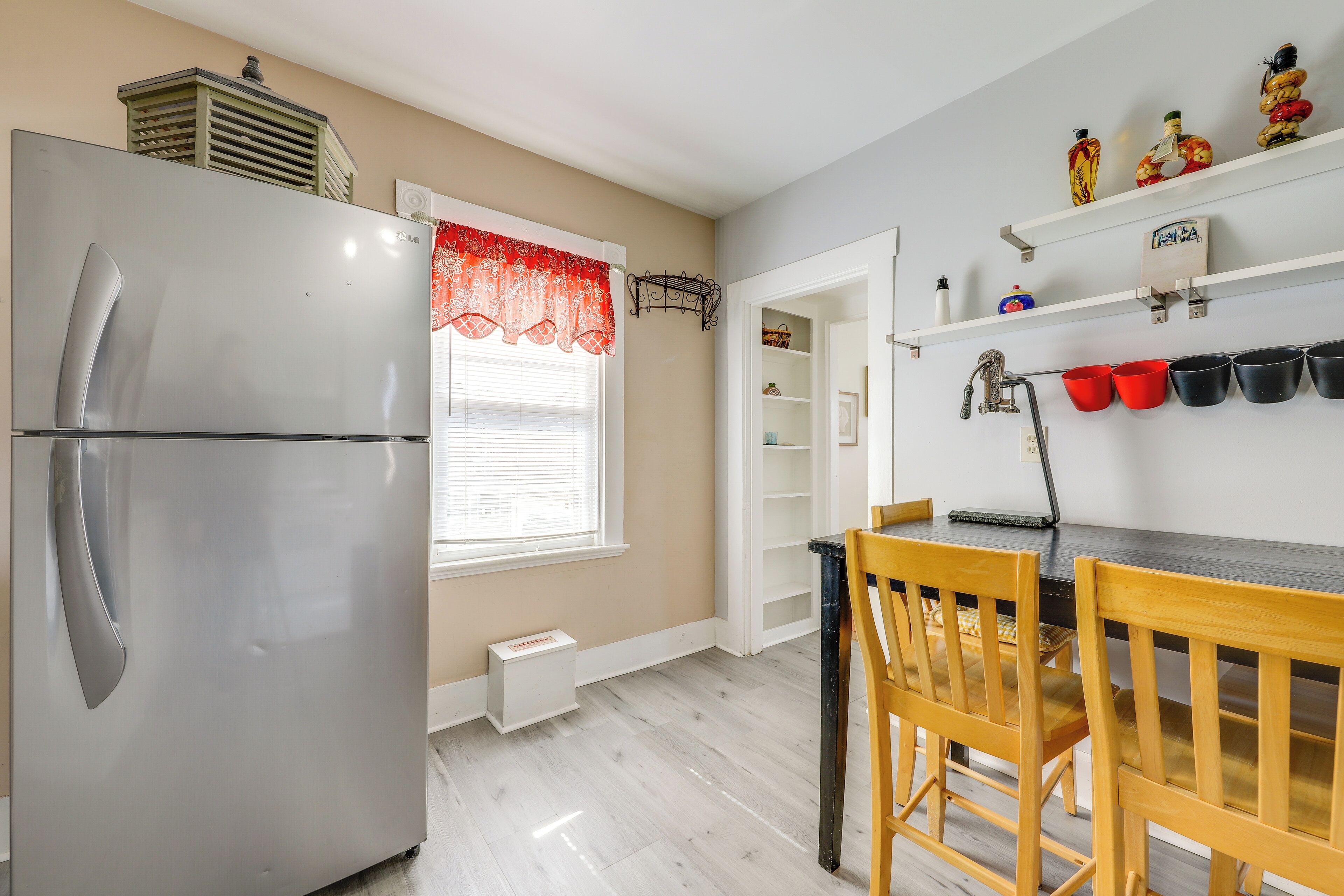 Una cocina con un refrigerador de acero inoxidable, sillas de madera y un ventanal con un adorno rojo.