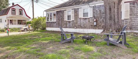 A house with a large tree in the yard, two outdoor chairs, and a wheelbarrow.