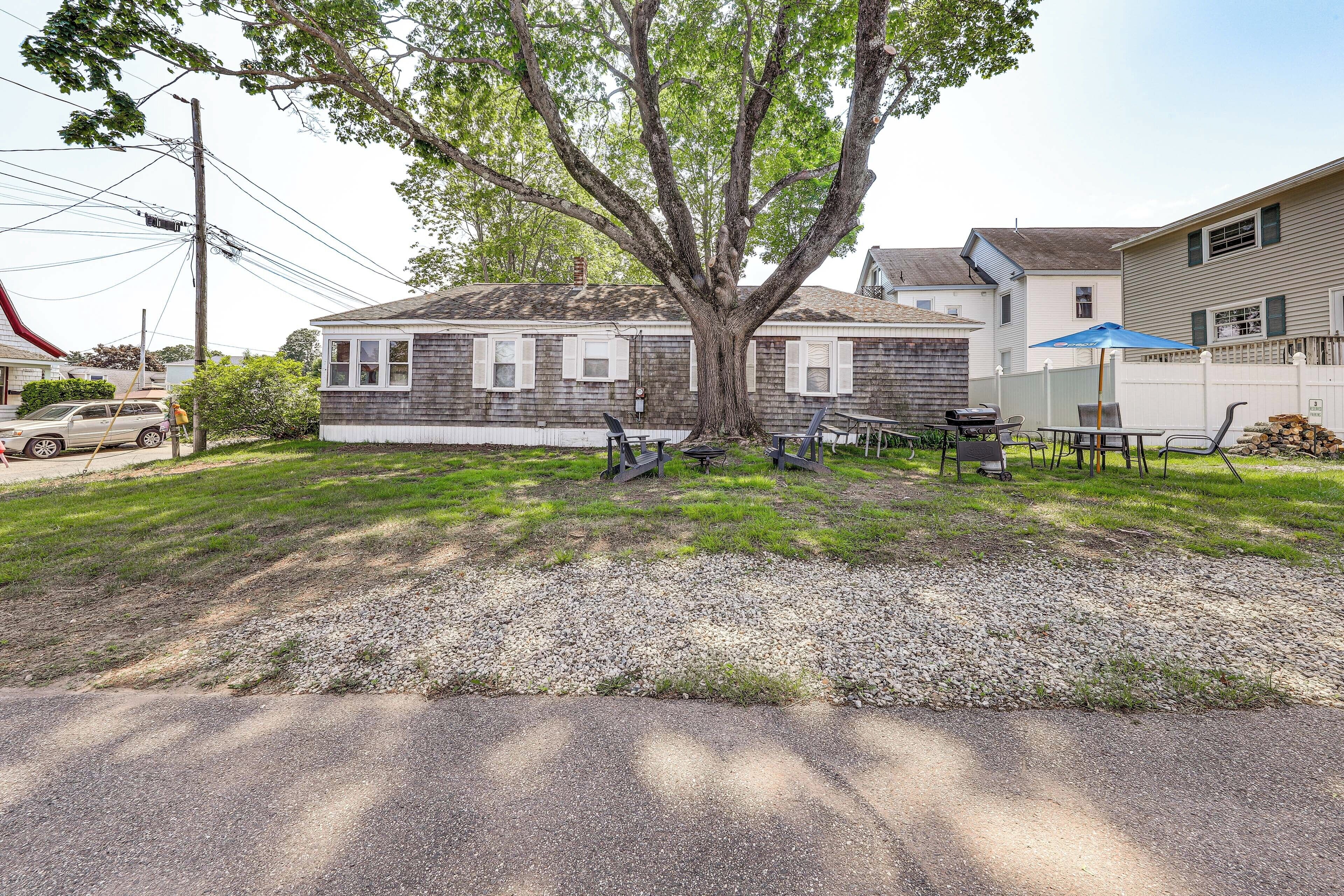 A house with a large tree in front, a gravel driveway, and a picnic table with chairs.
