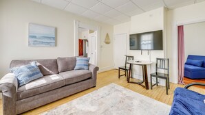 A living room with a sofa, a coffee table, and a TV. There is a door leading to another room. - 1/2 Mi to Ocean: Cozy Apt in Old Orchard Beach (Old Orchard Beach)