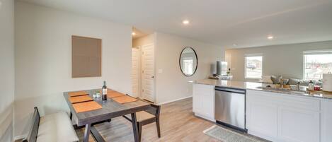 A modern kitchen with a dining area, white cabinetry, and a large window providing natural light.