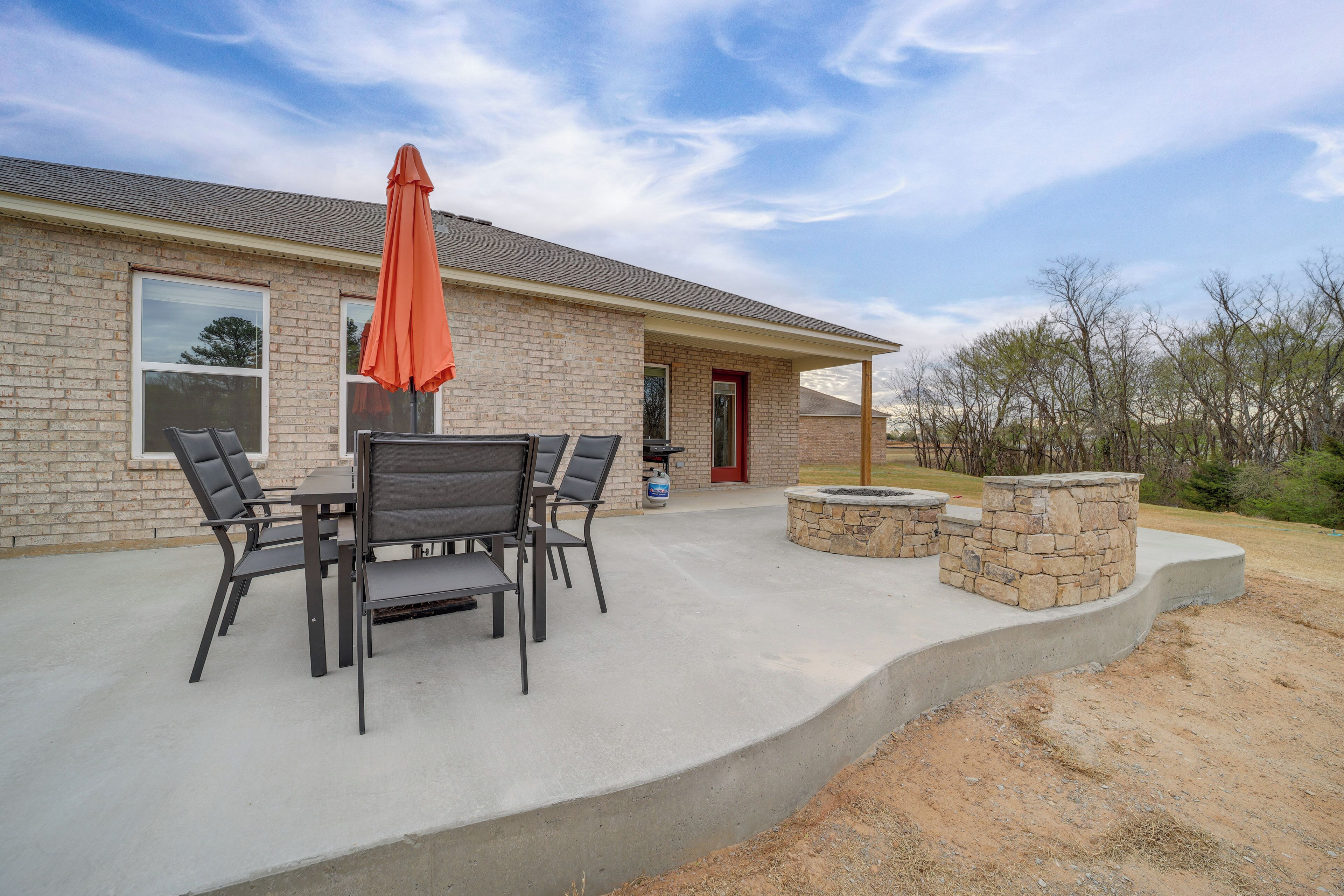 A patio with a table and chairs, a stone fire pit, and a brick house with a red door.
