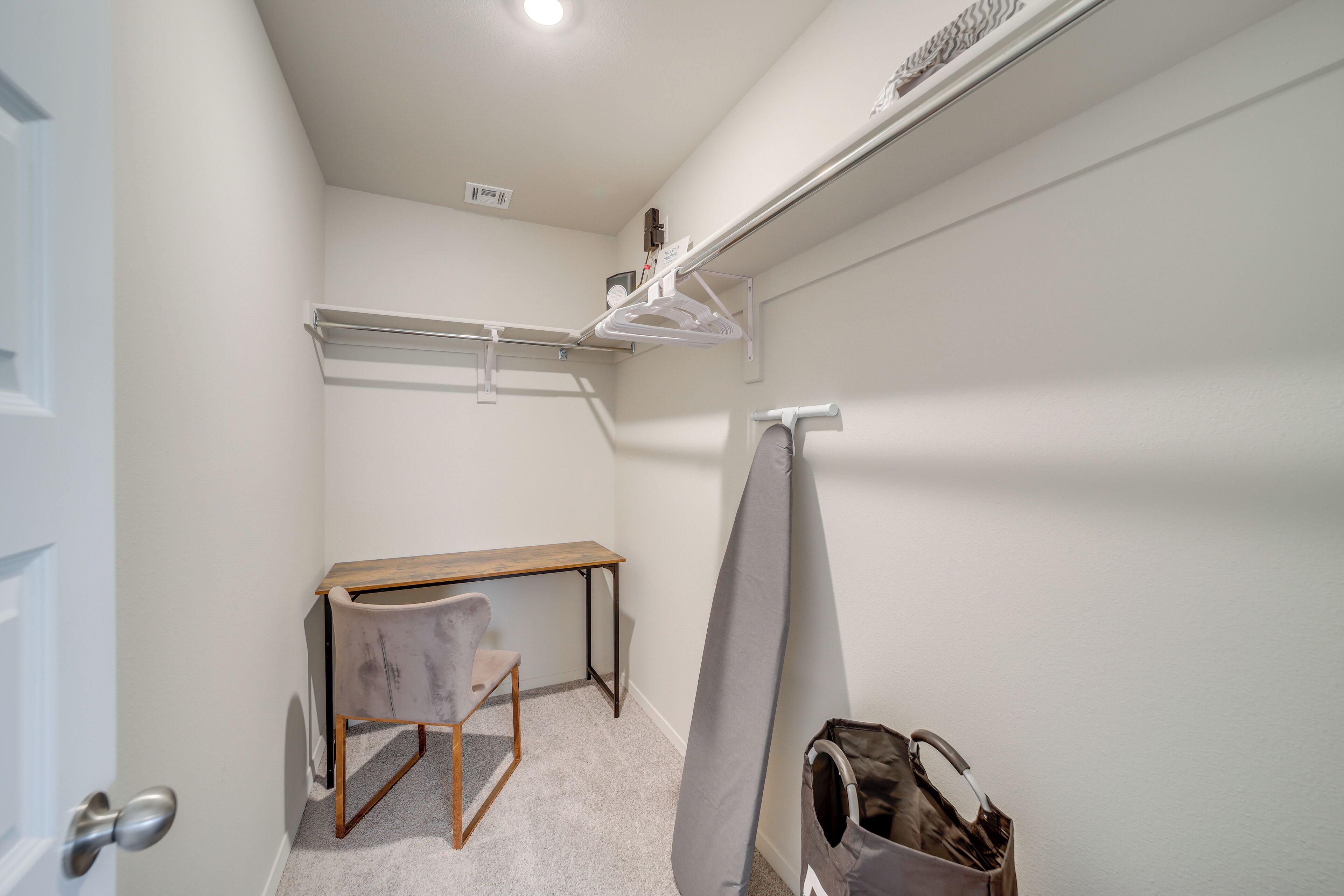 Une petite pièce, bien rangée, avec un bureau, une chaise et un portant à vêtements.