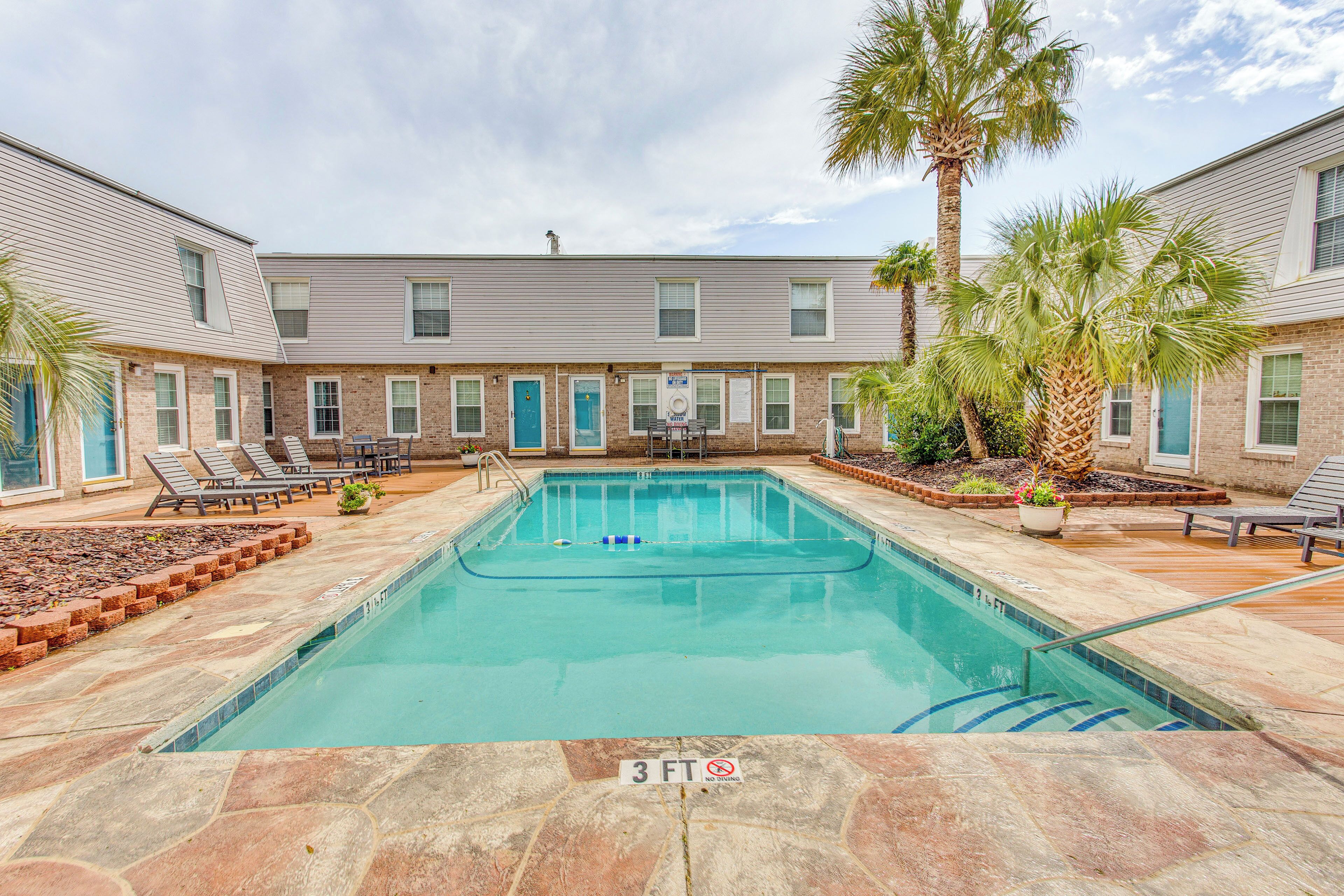 A rectangular pool with a 3 FT depth marker, surrounded by lounge chairs and palm trees, with a brick building in the background.