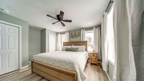 A bedroom with a wooden bed, a ceiling fan, a nightstand, and a window with curtains. - Walk to Lake: Pet-friendly Cottage in Jamestown! (Pymatuning South)