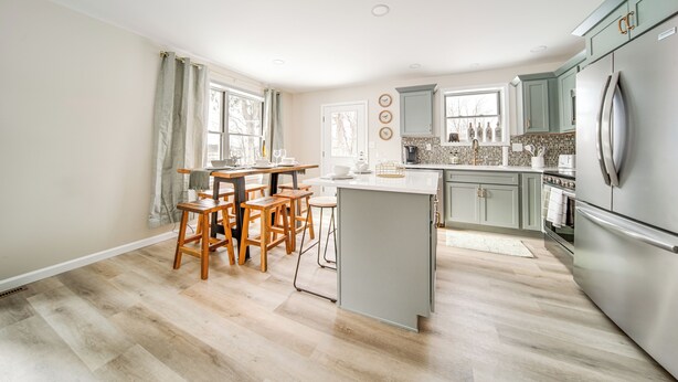 A modern kitchen with wooden chairs, a dining table, and a large island. - Walk to Lake: Pet-friendly Cottage in Jamestown! (Pymatuning South)