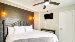 A neatly made bed with a metal headboard, a ceiling fan, and a mounted TV on the wall. - Walk to Casino: Home w/ Deck in Hot Springs! (Hot Springs)