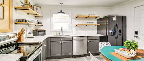 A modern kitchen with stainless steel appliances, wooden shelves, and a dining area with a green table.