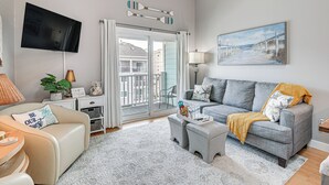 A living room with a grey sofa, a beige armchair, a coffee table, and a television mounted on the wall. - Walk to Beach: Condo w/ Balcony in Murrells Inlet! (Murrells Inlet)