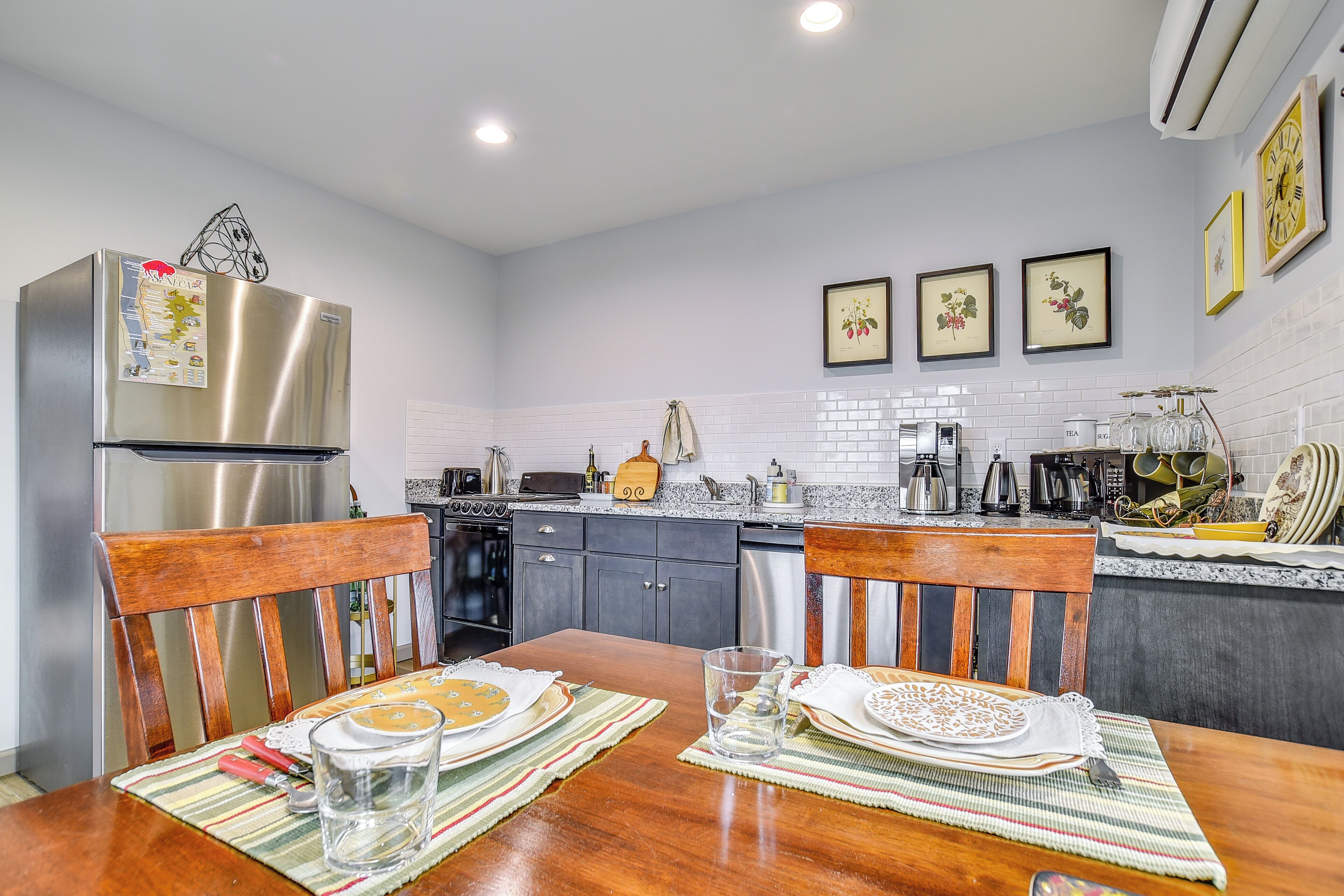 A modern kitchen with stainless steel appliances, a dining table set for two, and a tiled backsplash.