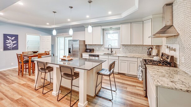 A modern kitchen with a central island, pendant lighting, and wooden flooring.