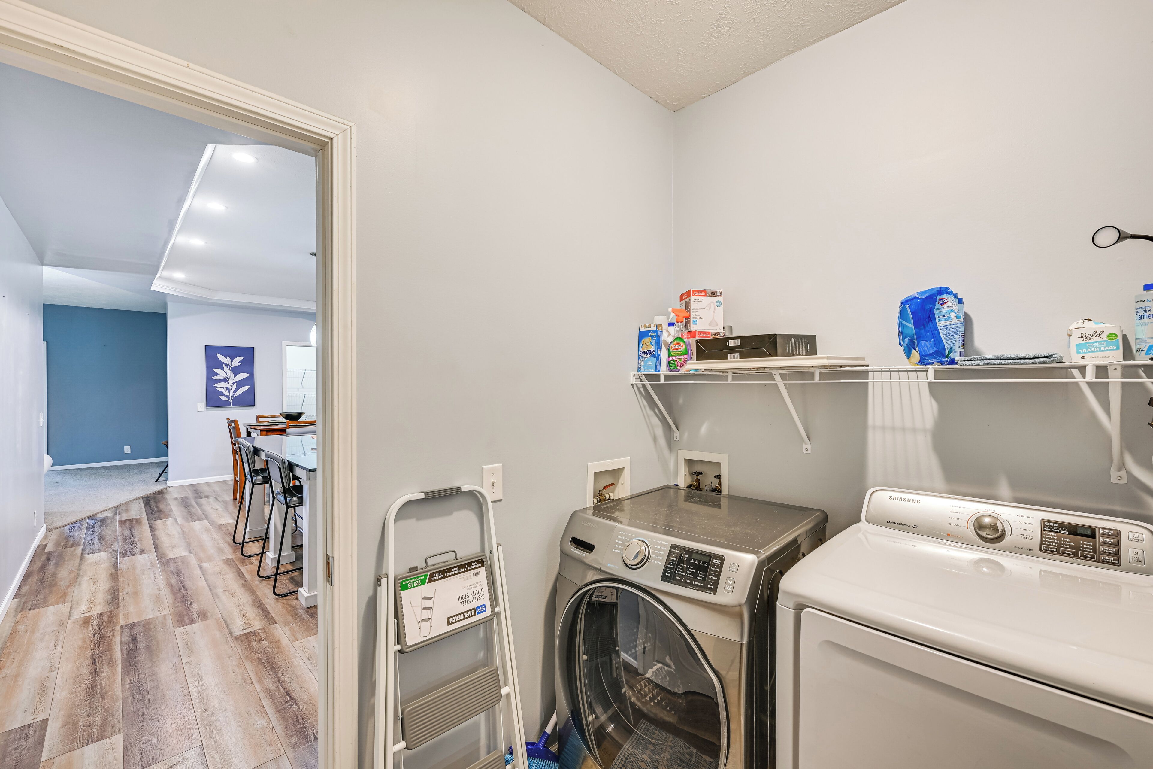 A laundry area with a washing machine, dryer, and shelves with cleaning supplies.