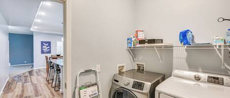 A laundry area with a washing machine, dryer, and shelves with cleaning supplies.