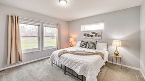 A bedroom with a bed, two bedside lamps, a window with curtains, and a wall-mounted picture.