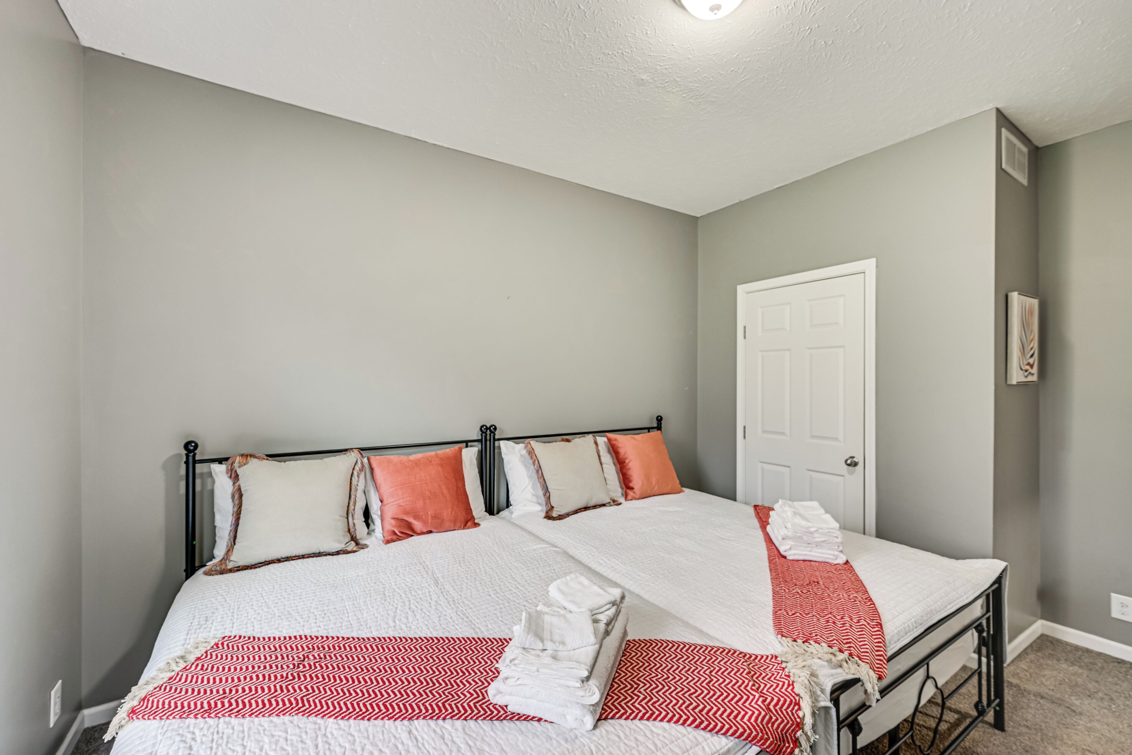 Un lit double avec une couvre-lit à motifs rouges et blancs, deux oreillers et une serviette blanche pliée, posée sur le côté.
