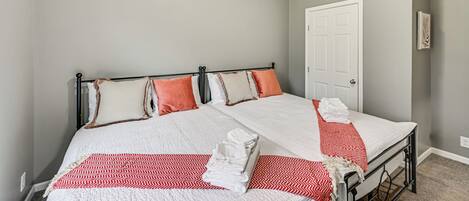 Un lit double avec une couvre-lit à motifs rouges et blancs, deux oreillers et une serviette blanche pliée, posée sur le côté.