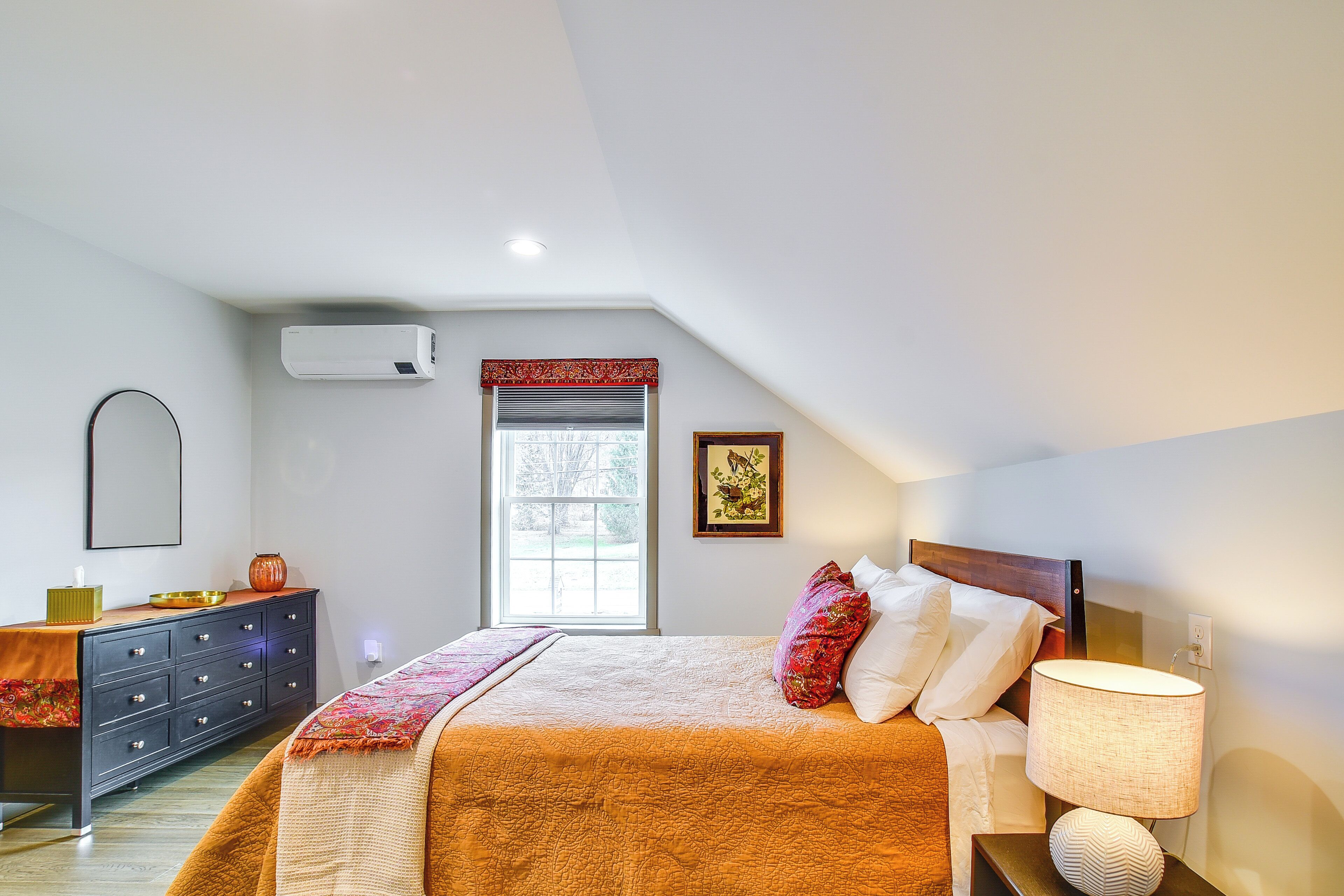 A bedroom with a bed, dresser, bedside lamp, window, and air conditioning unit.
