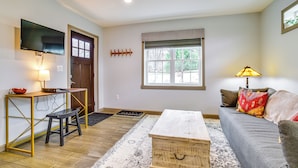 A living room with a sofa, a coffee table, a TV, a wooden bench, and a window with blinds. - Seneca Lake Wine Trail Studio w/ Balcony & Views! (Hector)