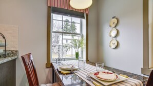 A kitchen with a dining table set for two, a window with a view of a house, and a wall-mounted plate rack. - Seneca Lake Wine Trail Studio w/ Balcony & Views! (Hector)