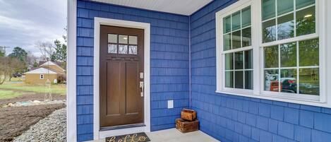 Una casa con fachada azul, puerta principal marrón y ventana blanca.