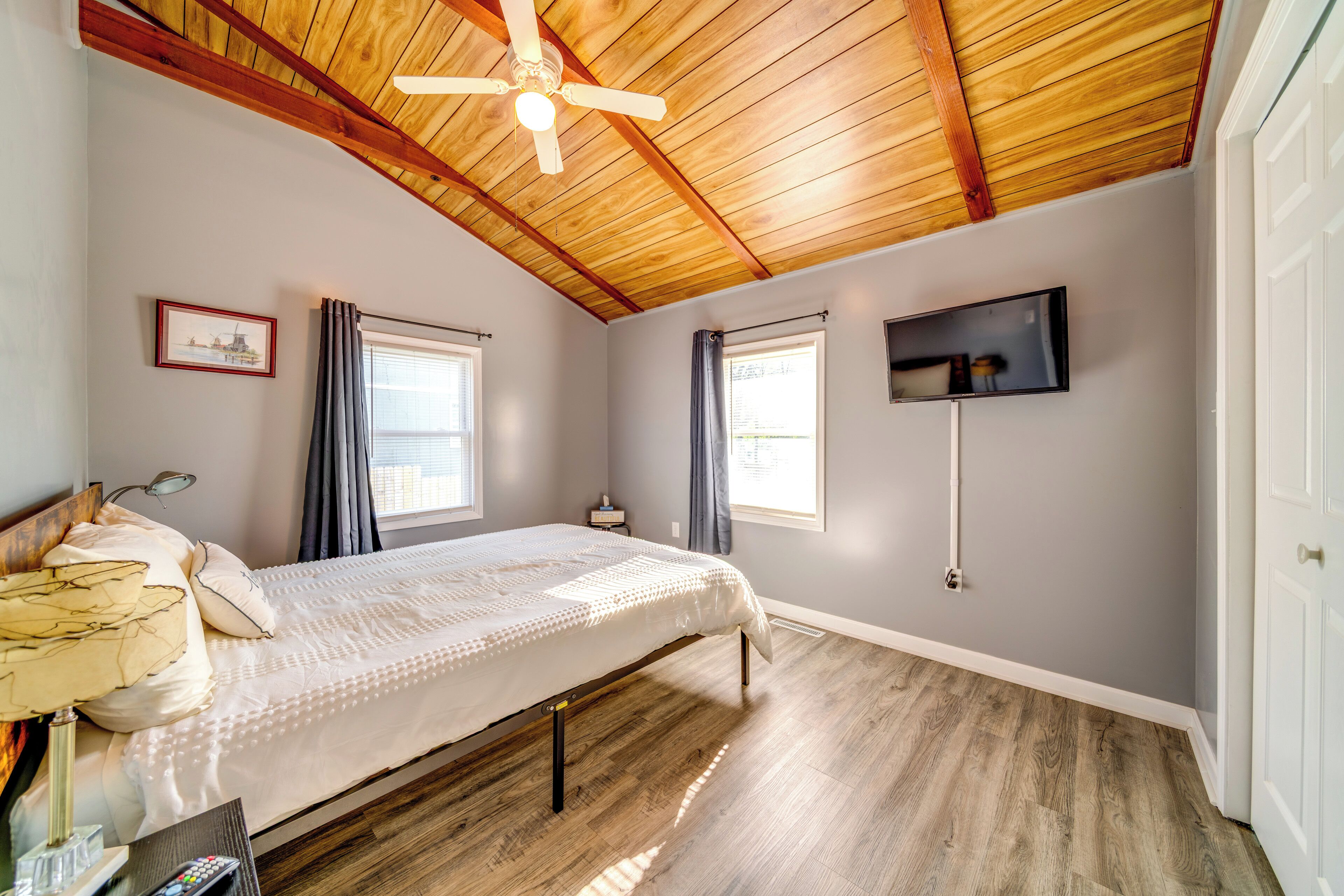 A bedroom with a bed, a ceiling fan, a TV, and a window.