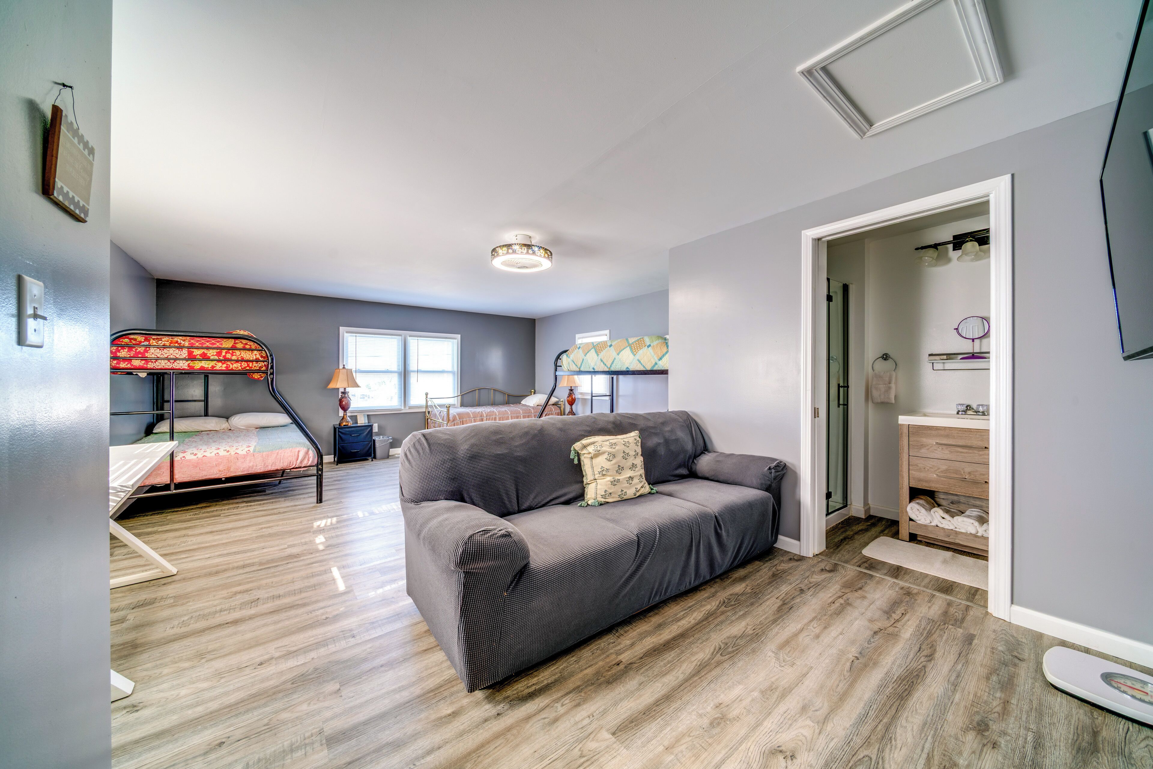 A room with a gray sofa, a bunk bed, a wooden floor, a ceiling light, and a closet with shelves.
