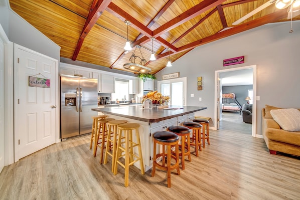 A spacious kitchen with a large island, wooden stools, and a stainless steel refrigerator.