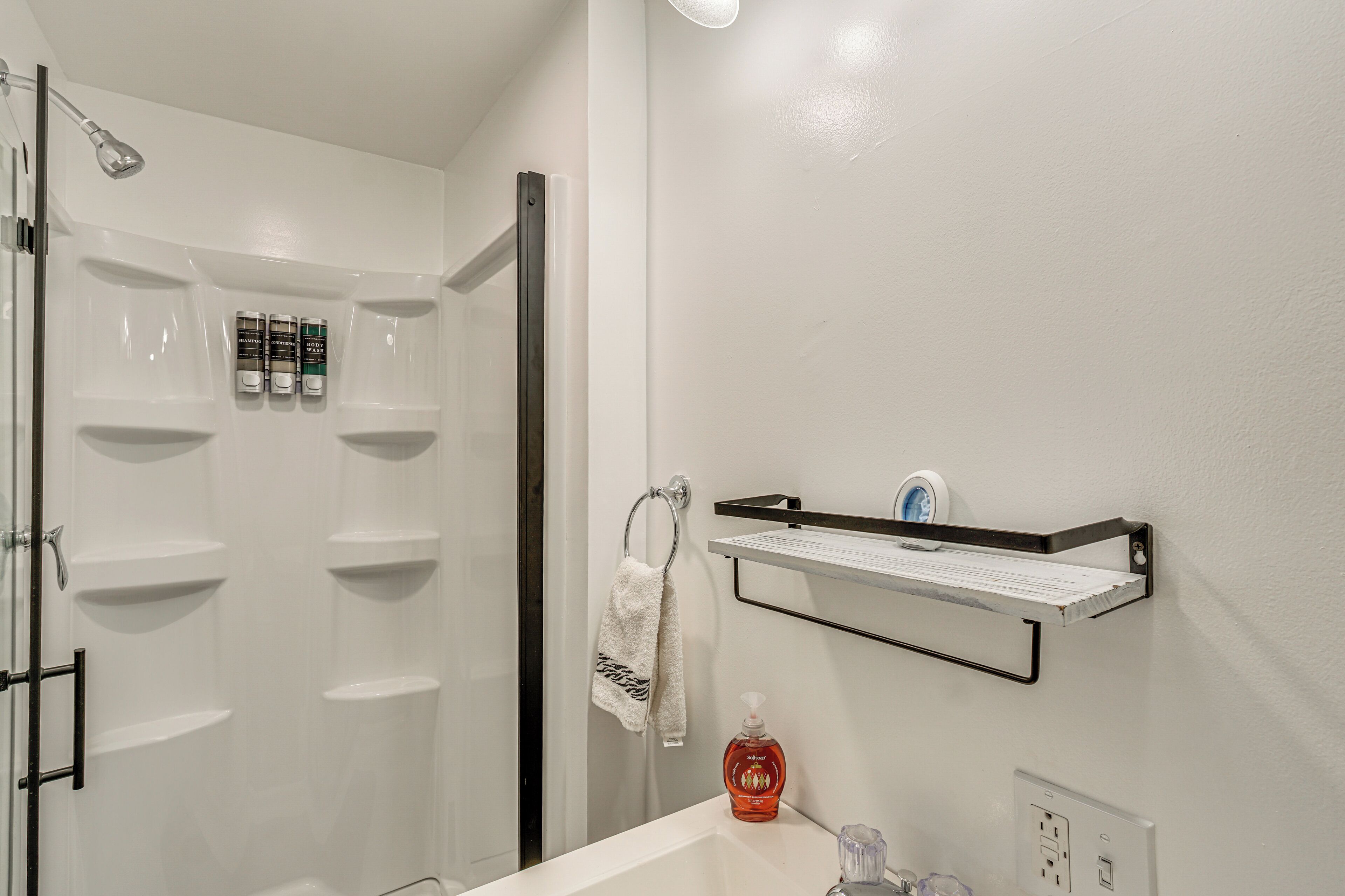 A modern bathroom with a shower, a sink, and a shelf with toiletries.