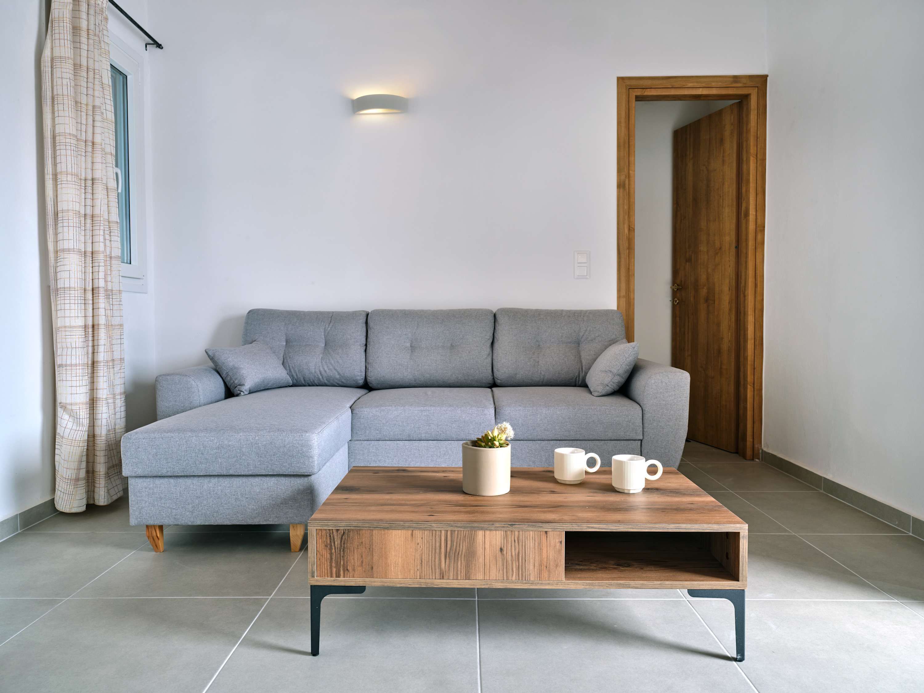 Ein modernes Wohnzimmer mit einem grauen Ecksofa, einem Holztisch und einer kleinen Zimmerpflanze.