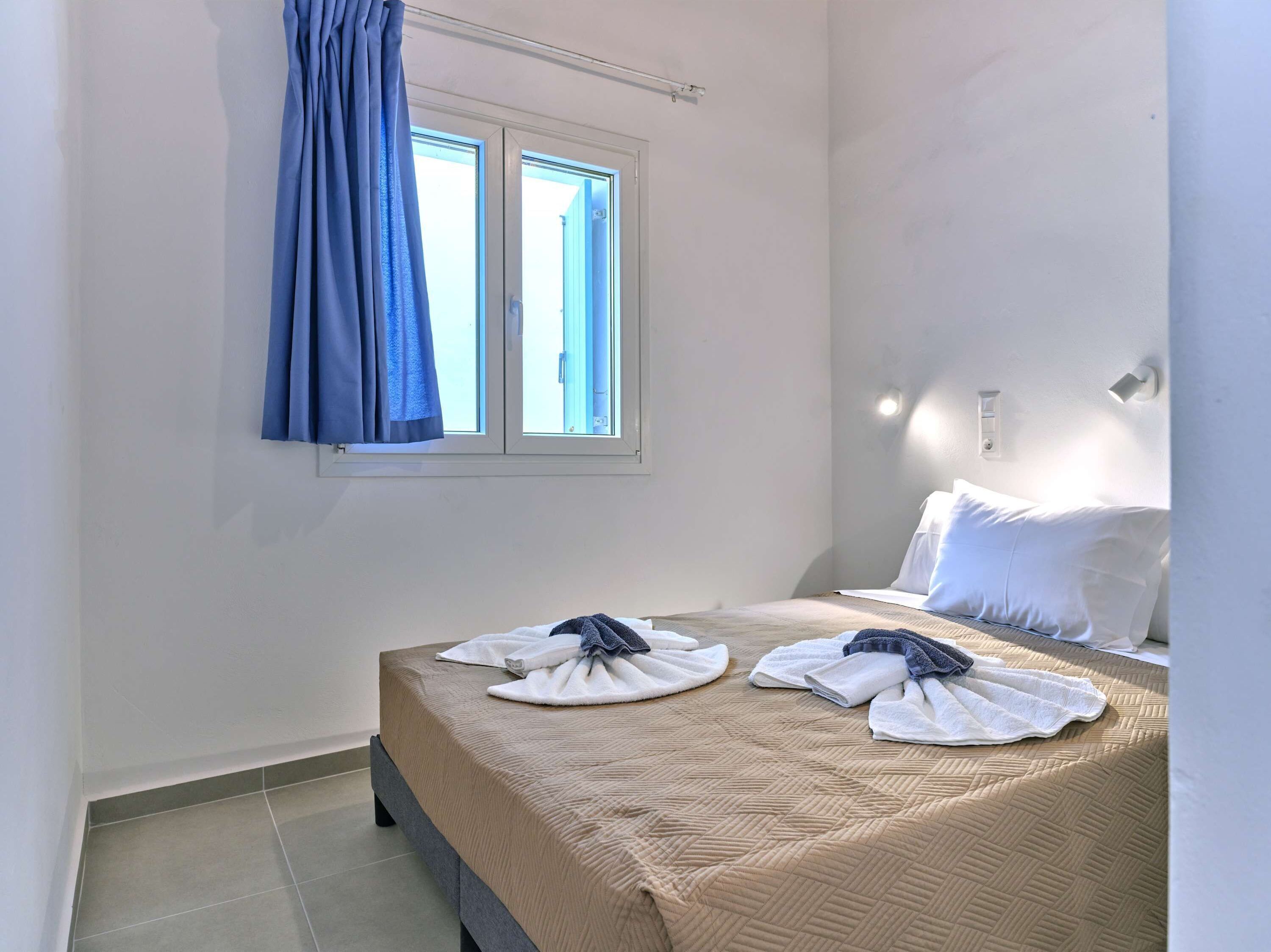 A hotel room with a bed, a window with blue curtains, and a wall-mounted light fixture.