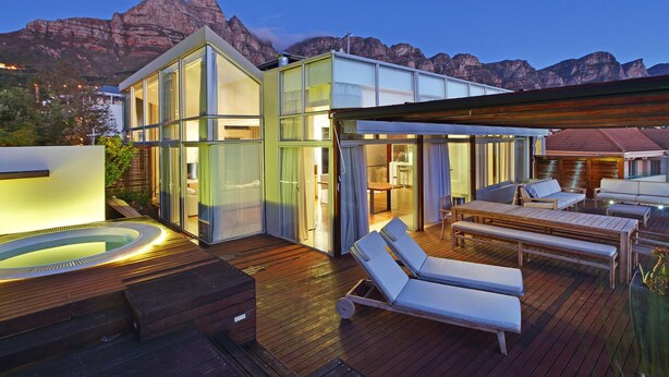 Une terrasse extérieure moderne, dotée de chaises longues et d’un jacuzzi, offrant une vue sur un paysage montagneux.