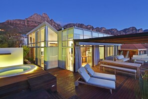 Una terrazza esterna moderna con poltrone relax e una vasca idromassaggio, con vista su un paesaggio montuoso.