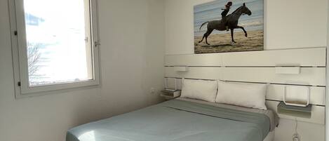 Ein Schlafzimmer mit Bett, Fenster, einem Bild und einem Nachttisch.