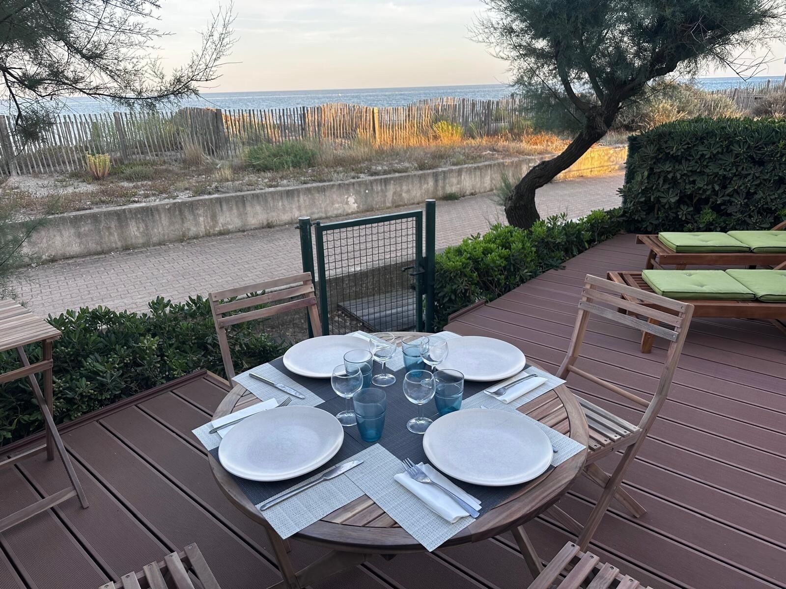 A round table set for four with plates, cutlery, and glasses, overlooking a beach.