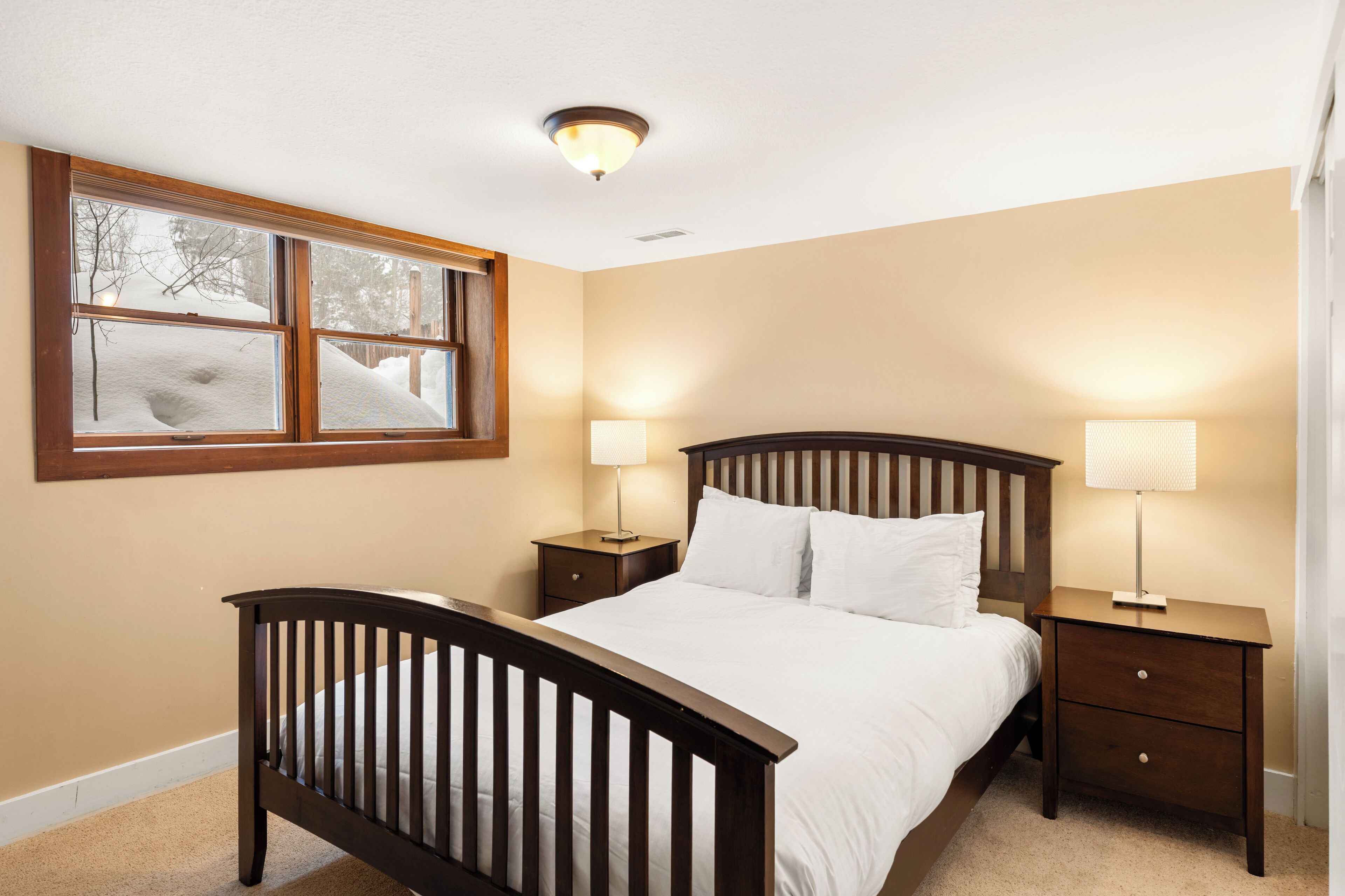 A bedroom with a wooden bed, two bedside tables, and a window with a view of snow-covered trees.
